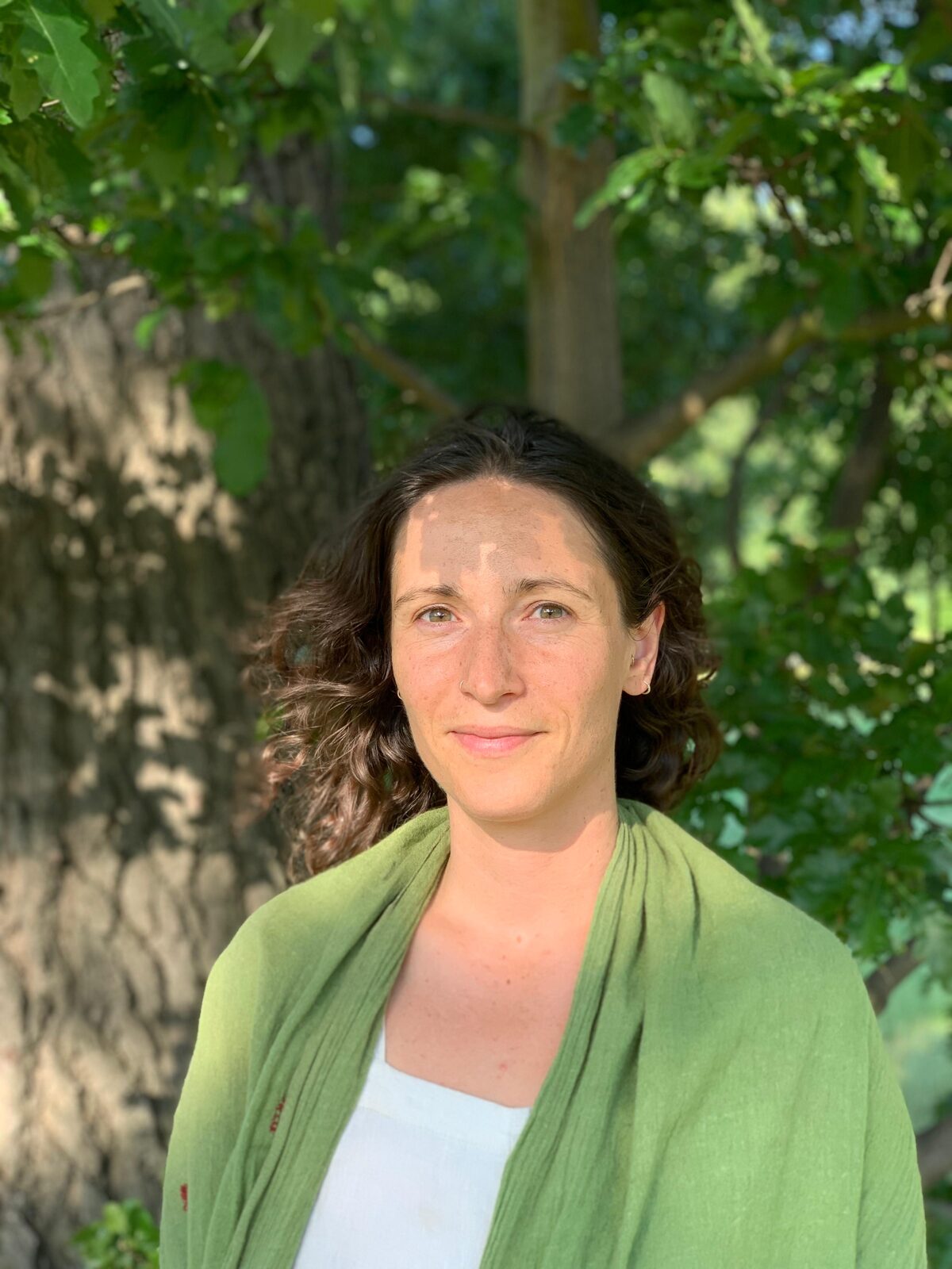 Emily, craniosacral therapist, standing beneath a tree in a green shawl