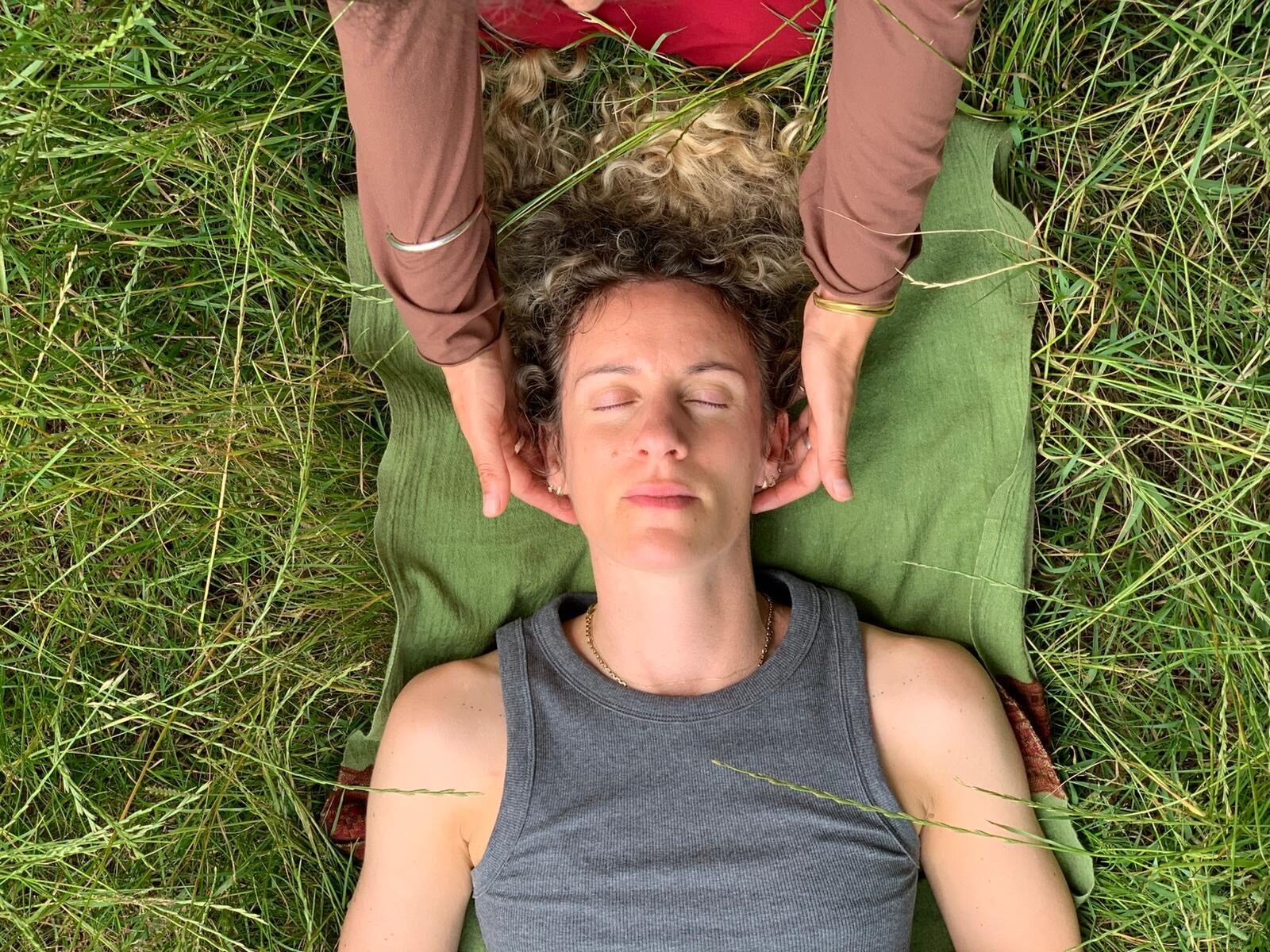 Craniosacral therapy treatment, a practitioner cradling a person's head in a meadow